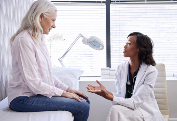 Dermatologist visit Skin Cancer Foundation Mature Woman In Consultation for a melanoma treatment With Female Doctor Sitting On Examination Couch In Office